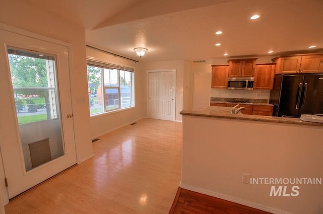 kitchen with sink, light wood-type flooring, black refrigerator, and stone countertops