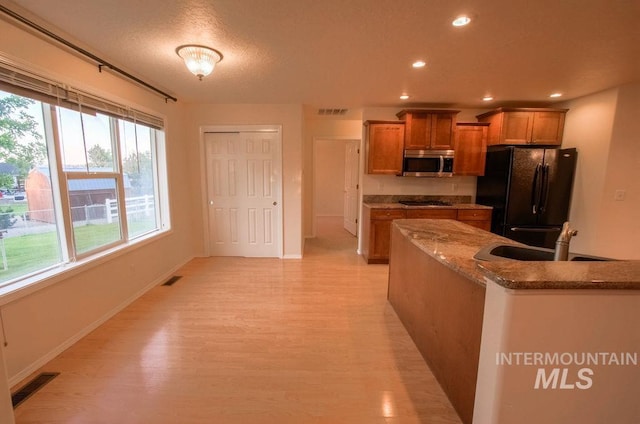 kitchen featuring dark stone countertops, light hardwood / wood-style flooring, sink, a textured ceiling, and black refrigerator