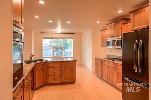 kitchen featuring sink, black appliances, light stone countertops, and light wood-type flooring