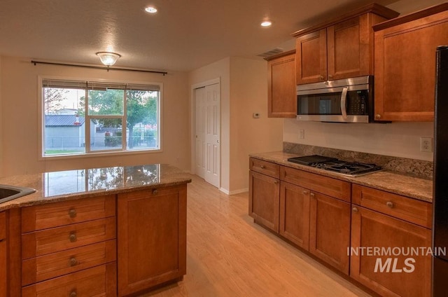 kitchen with light hardwood / wood-style floors, appliances with stainless steel finishes, and light stone counters