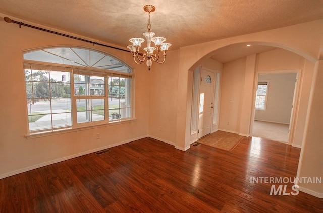 spare room featuring an inviting chandelier, dark wood-type flooring, and a textured ceiling