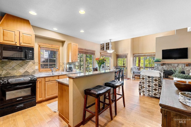 kitchen with light stone counters, sink, black appliances, light brown cabinets, and a stone fireplace