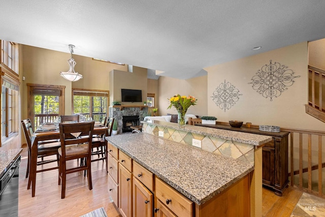 kitchen with a stone fireplace, light hardwood / wood-style flooring, light stone countertops, decorative light fixtures, and a kitchen island