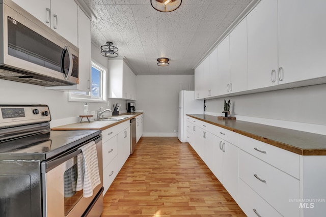 kitchen featuring ornamental molding, a sink, appliances with stainless steel finishes, white cabinets, and light wood finished floors