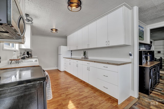 kitchen with stainless steel microwave, electric range oven, white cabinetry, freestanding refrigerator, and light wood-style floors