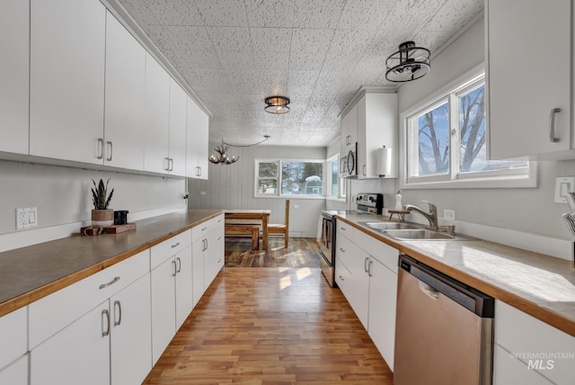 kitchen featuring white cabinets, appliances with stainless steel finishes, light wood-type flooring, and a sink