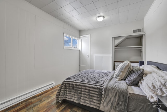 bedroom featuring visible vents, baseboard heating, a closet, and wood finished floors