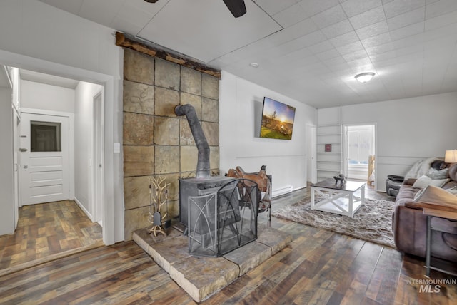 living area featuring a wood stove, built in shelves, wood finished floors, and ceiling fan