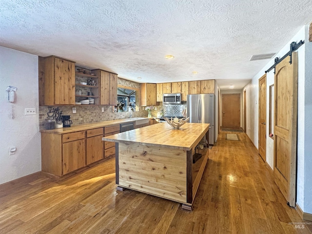 kitchen featuring a barn door, hardwood / wood-style flooring, stainless steel appliances, a center island, and sink