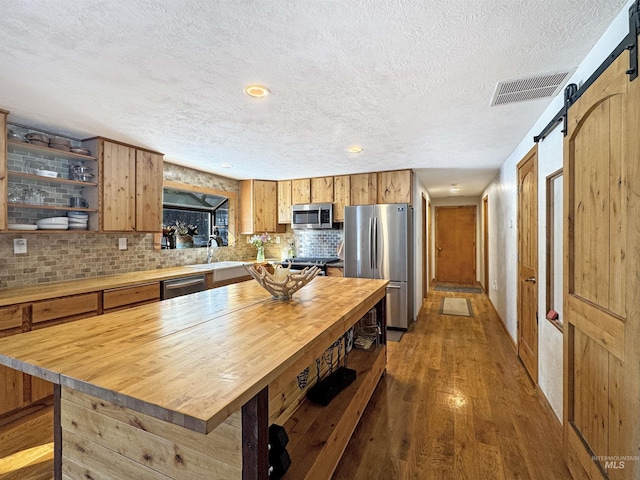 kitchen with tasteful backsplash, a barn door, a center island, hardwood / wood-style floors, and appliances with stainless steel finishes