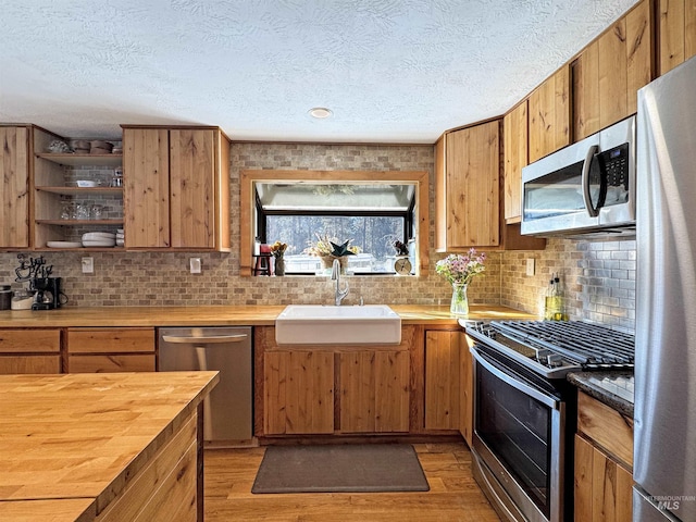 kitchen with sink, a textured ceiling, appliances with stainless steel finishes, and light hardwood / wood-style flooring