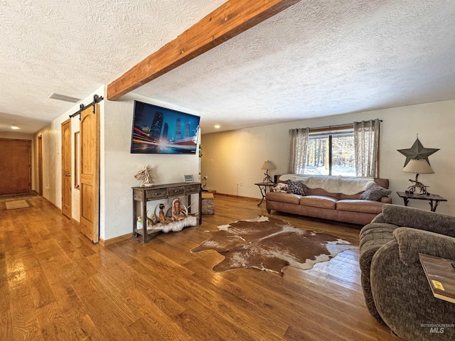 living room with hardwood / wood-style flooring, a textured ceiling, beam ceiling, and a barn door