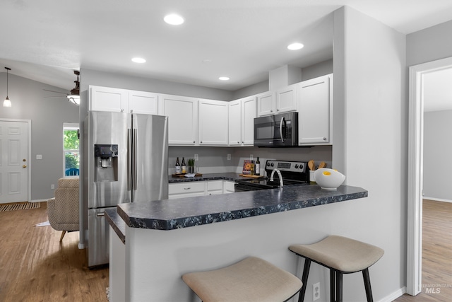11031 W Red Maple Dr, Boise, ID 83709 - kitchen featuring appliances with stainless steel finishes, a peninsula, white cabinets, wood finished floors, and dark countertops