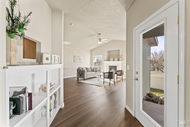 interior space featuring a warm lit fireplace, lofted ceiling, ceiling fan, dark wood-type flooring, and a textured ceiling