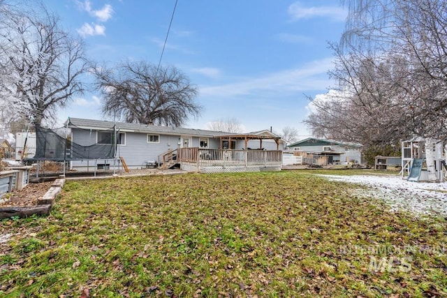 back of property featuring a deck, a trampoline, and a yard