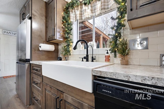 kitchen featuring dark brown cabinetry, dishwasher, sink, light hardwood / wood-style floors, and a textured ceiling