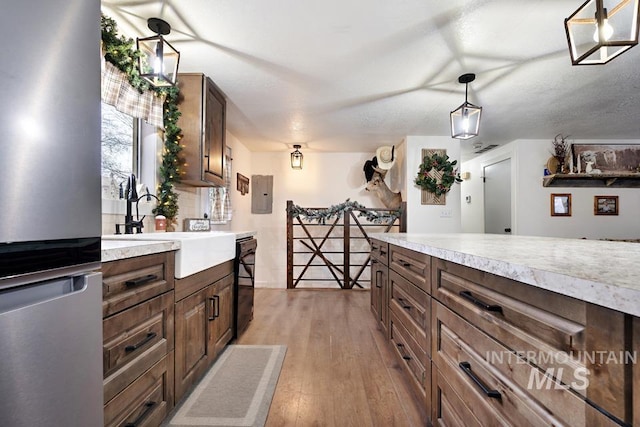 kitchen with a textured ceiling, sink, decorative light fixtures, light hardwood / wood-style flooring, and dishwasher