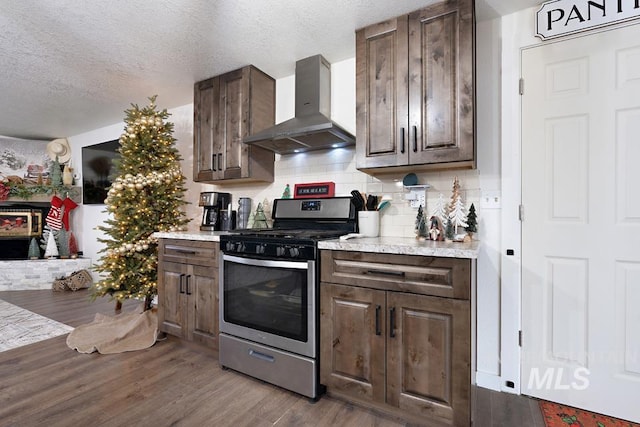 kitchen with stainless steel gas stove, dark brown cabinets, wall chimney range hood, and light hardwood / wood-style flooring