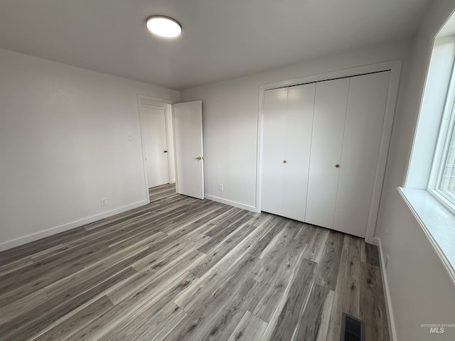 unfurnished bedroom featuring a closet, visible vents, baseboards, and wood finished floors