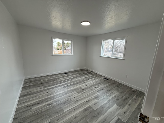 unfurnished room with visible vents, a textured ceiling, baseboards, and wood finished floors