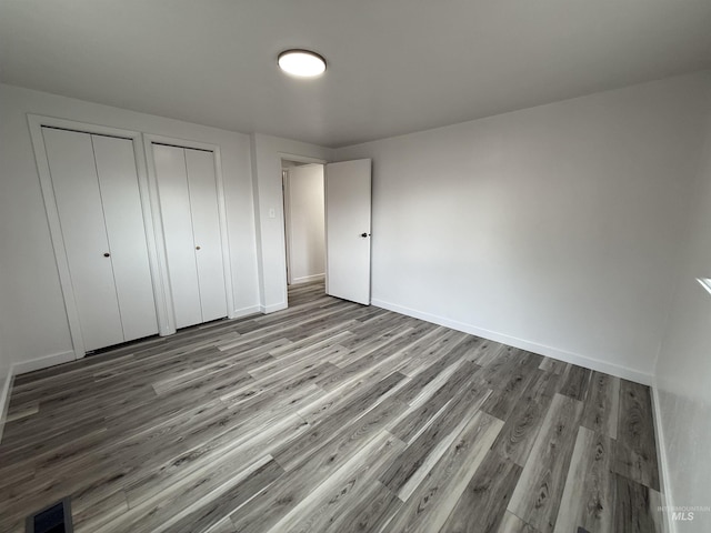 unfurnished bedroom featuring visible vents, two closets, baseboards, and wood finished floors