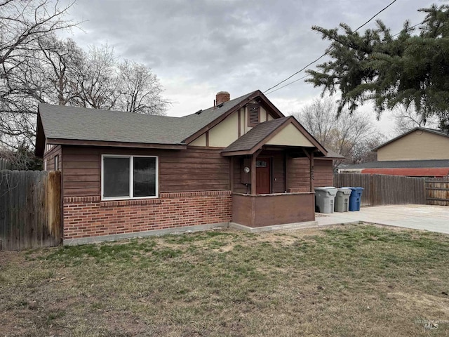 view of front of home with a front lawn, fence, brick siding, and a shingled roof