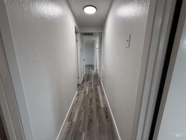 corridor with wood finished floors, baseboards, and a textured wall