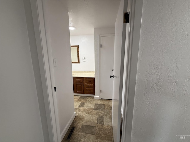 hallway featuring visible vents, stone finish floor, baseboards, and a textured wall