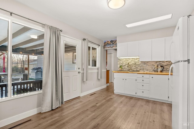 kitchen with backsplash, white fridge, light hardwood / wood-style floors, sink, and white cabinets