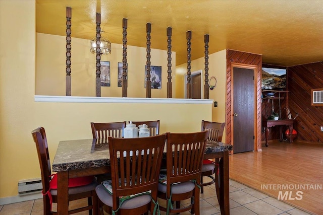 dining room featuring wooden walls, a baseboard heating unit, and tile patterned floors