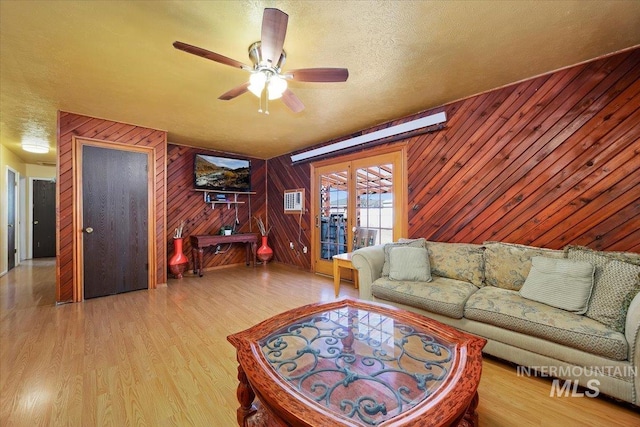 living area featuring a textured ceiling, ceiling fan, wood finished floors, and wooden walls