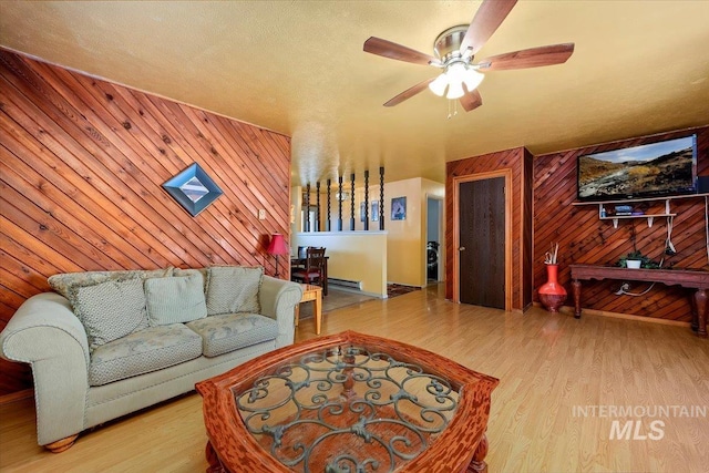 living room with wooden walls, a ceiling fan, and wood finished floors