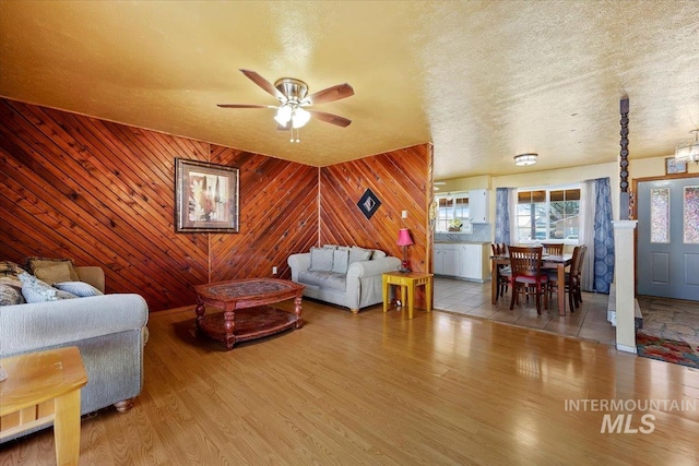 living area featuring a ceiling fan, wood walls, a textured ceiling, and wood finished floors