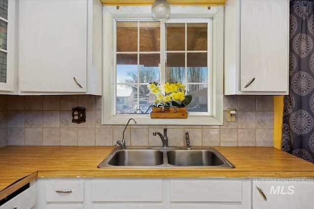 kitchen featuring wooden counters, white cabinetry, decorative backsplash, and a sink