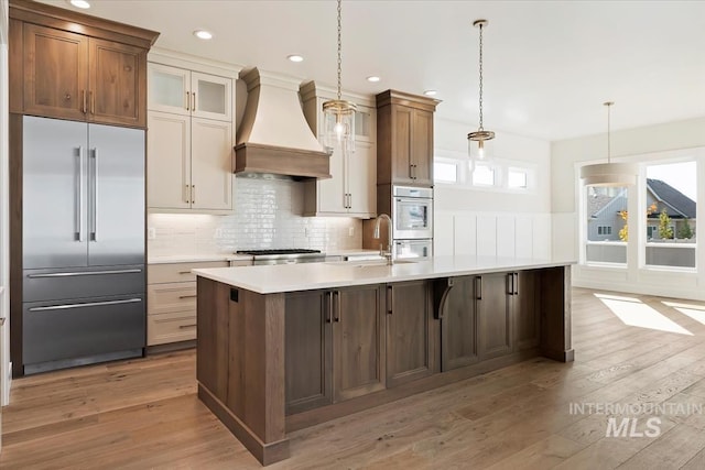 kitchen featuring decorative light fixtures, custom exhaust hood, stainless steel appliances, and a center island with sink