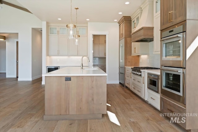 kitchen with pendant lighting, sink, stainless steel appliances, an island with sink, and custom exhaust hood