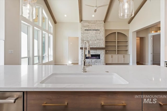 kitchen with a fireplace, decorative light fixtures, sink, light stone counters, and beam ceiling