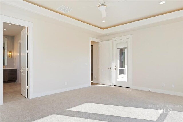 empty room with light carpet, ceiling fan, and a tray ceiling