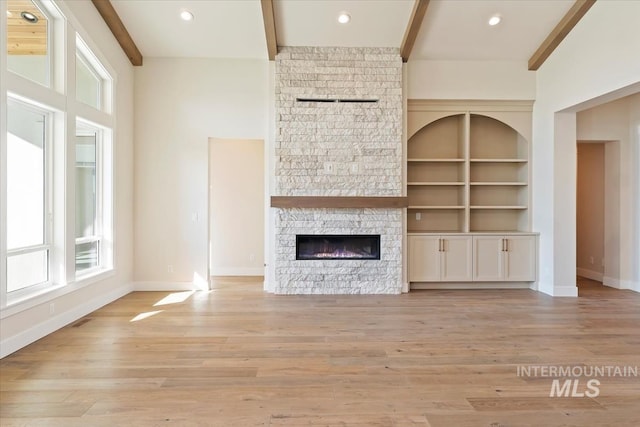 unfurnished living room featuring a towering ceiling, beam ceiling, a stone fireplace, and light wood-type flooring