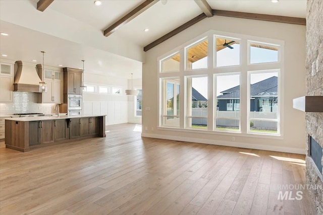 unfurnished living room featuring sink, high vaulted ceiling, a fireplace, light hardwood / wood-style floors, and beamed ceiling