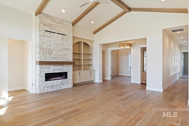 unfurnished living room with beam ceiling, a stone fireplace, high vaulted ceiling, and light hardwood / wood-style flooring