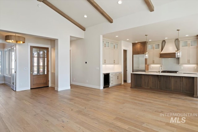 kitchen featuring custom exhaust hood, decorative light fixtures, stainless steel built in fridge, beam ceiling, and light hardwood / wood-style floors