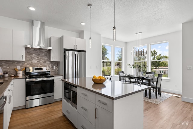509 E Violets Cove Ln, Garden City, ID 83714 - kitchen featuring tasteful backsplash, a center island, wall chimney exhaust hood, appliances with stainless steel finishes, and light wood finished floors