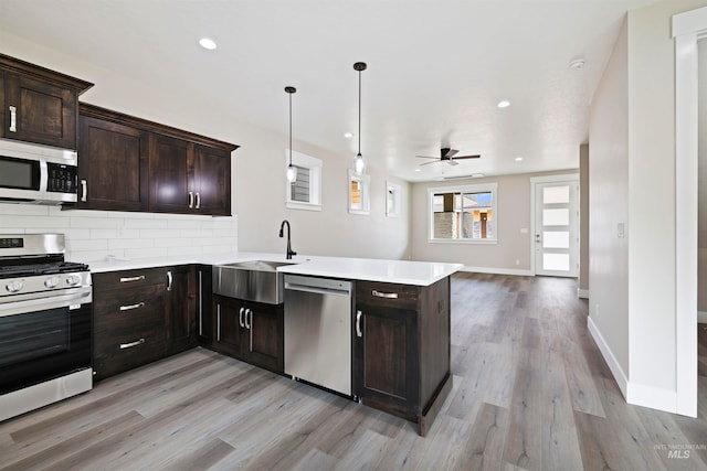 kitchen featuring stainless steel appliances, light hardwood / wood-style floors, kitchen peninsula, sink, and pendant lighting