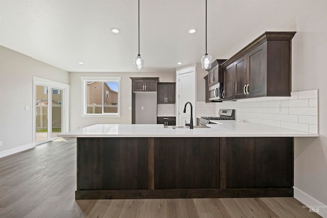 kitchen with stainless steel appliances, decorative light fixtures, sink, hardwood / wood-style flooring, and kitchen peninsula