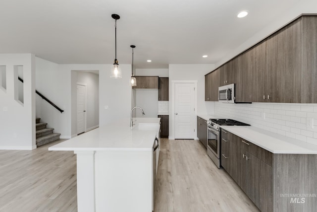 kitchen featuring light wood-style flooring, a sink, backsplash, light countertops, and appliances with stainless steel finishes