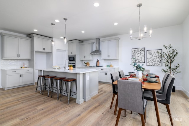 kitchen featuring pendant lighting, wall chimney exhaust hood, stainless steel appliances, and light hardwood / wood-style flooring