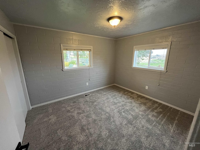 carpeted empty room featuring a textured ceiling, visible vents, brick wall, and baseboards
