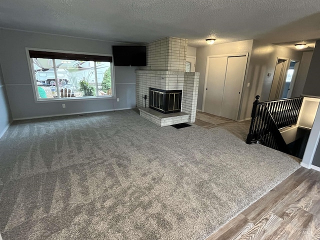 unfurnished living room featuring a brick fireplace, a textured ceiling, wood finished floors, and baseboards
