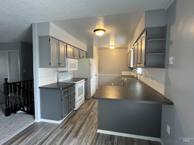 kitchen with a sink, dark wood-type flooring, a peninsula, white appliances, and dark countertops